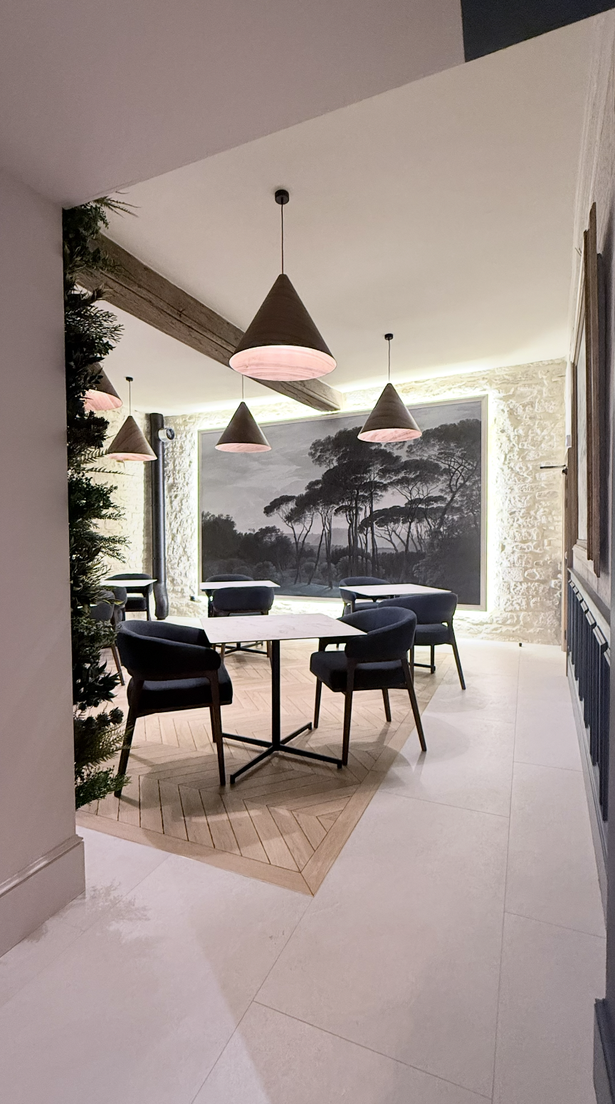Salle du restaurant Le Jean Maurice à Chablis aménagée par JBB architecte d’intérieur, avec panneau acoustique grand format paysage, mur en pierre apparente, parquet en chevrons et suspensions coniques en bois.