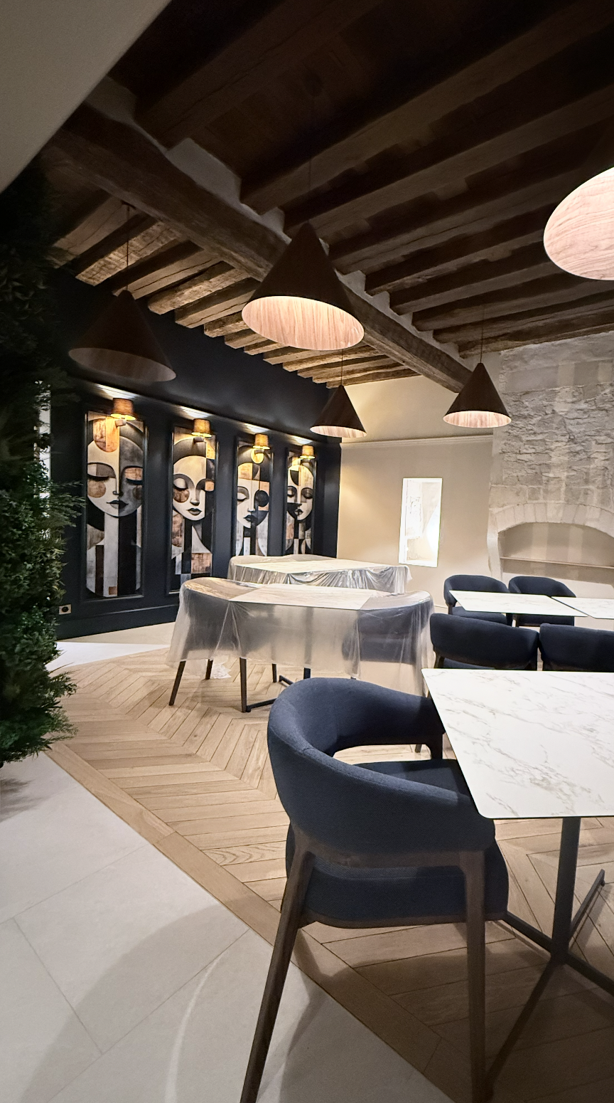 Tableaux acoustiques muraux conçus par JBB architecte d’intérieur pour le restaurant Le Jean Maurice à Chablis, intégrés dans une salle avec poutres apparentes, parquet en chevrons et éclairage chaleureux.
