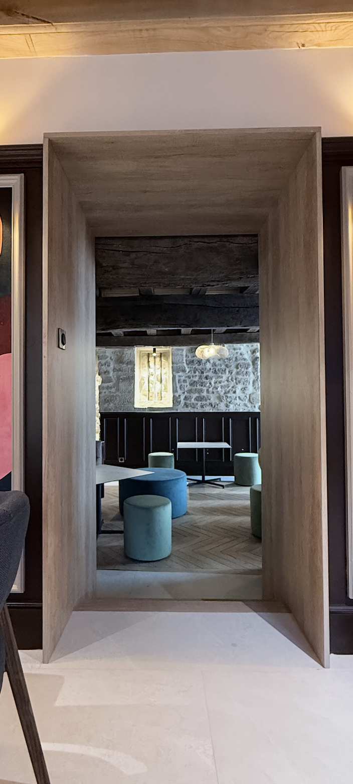 Perspective encadrée en bois ouvrant sur un salon de dégustation avec poufs velours vert et parquet chevrons, architecture intérieure JBB